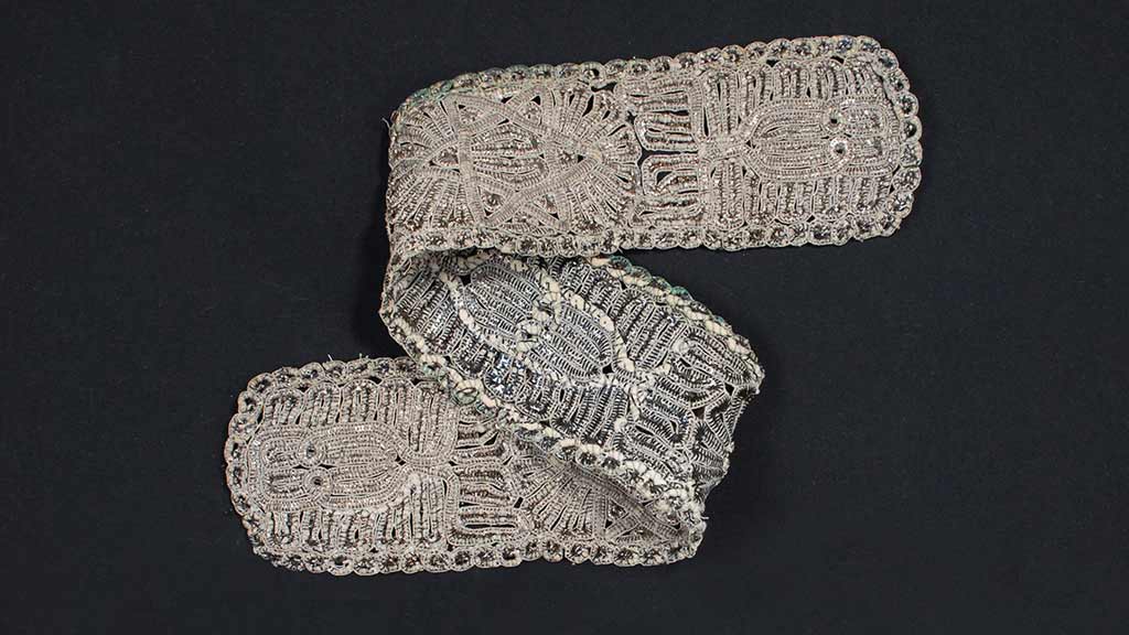 A folded fabric strip with intricate metallic embroidery