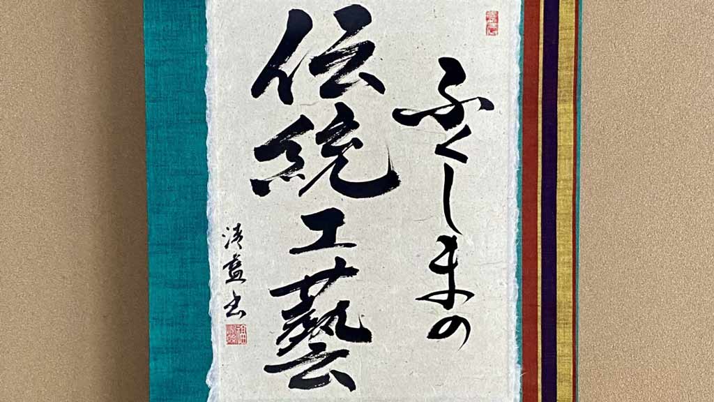 Japanese characters written in black ink on a scroll with colorful borders