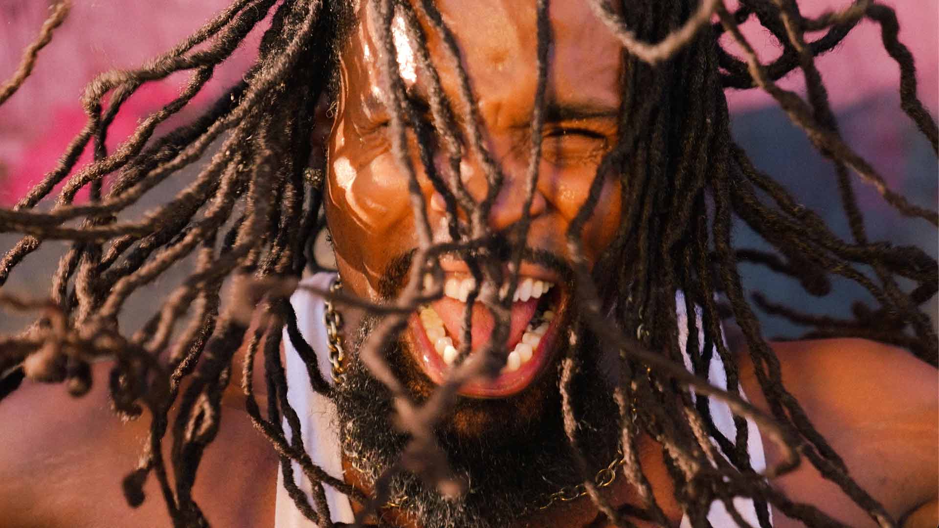 A closeup of a man with long hair braids in motion looking at camera squinting and shouting