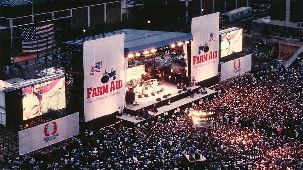 outdoor concert venue with Farm Aid signs and a sea of people