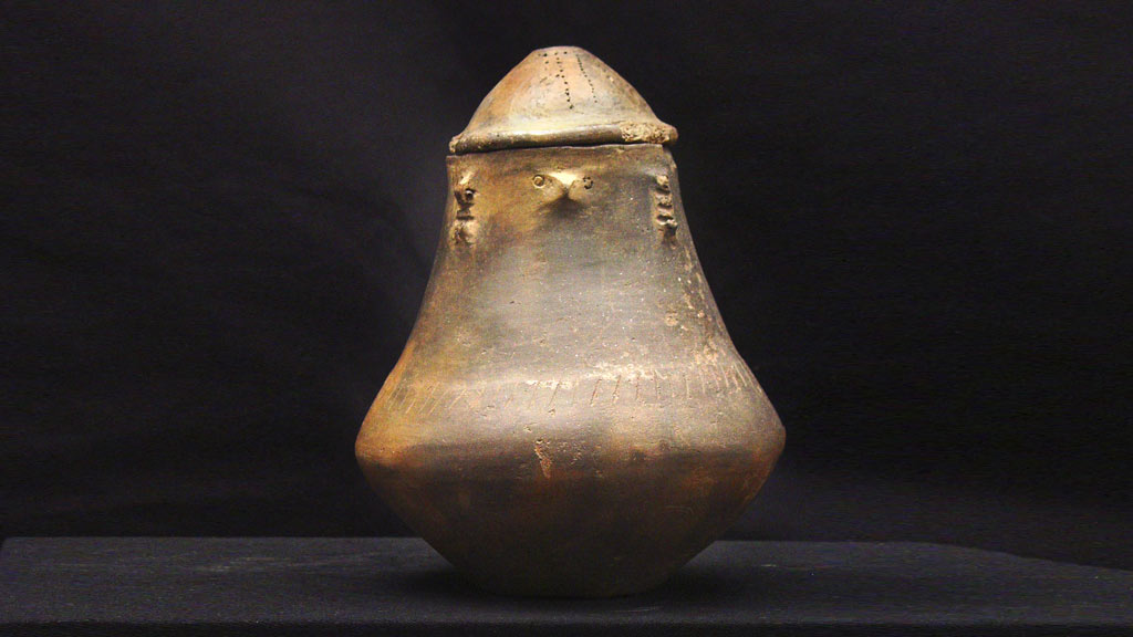 Tan and gray urn with stylized human faces around the upper lip