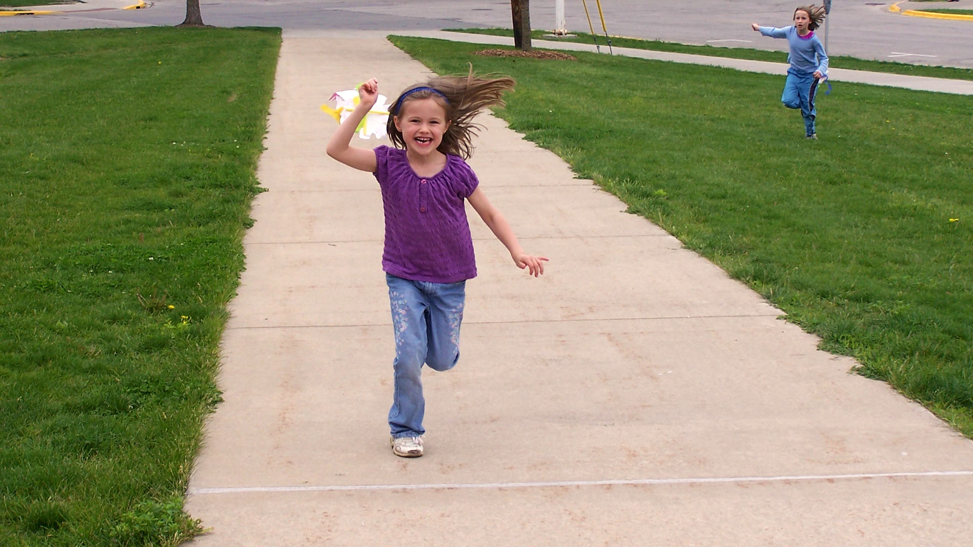Enthusiastic child running outdoors towards you with a kite catching wind
