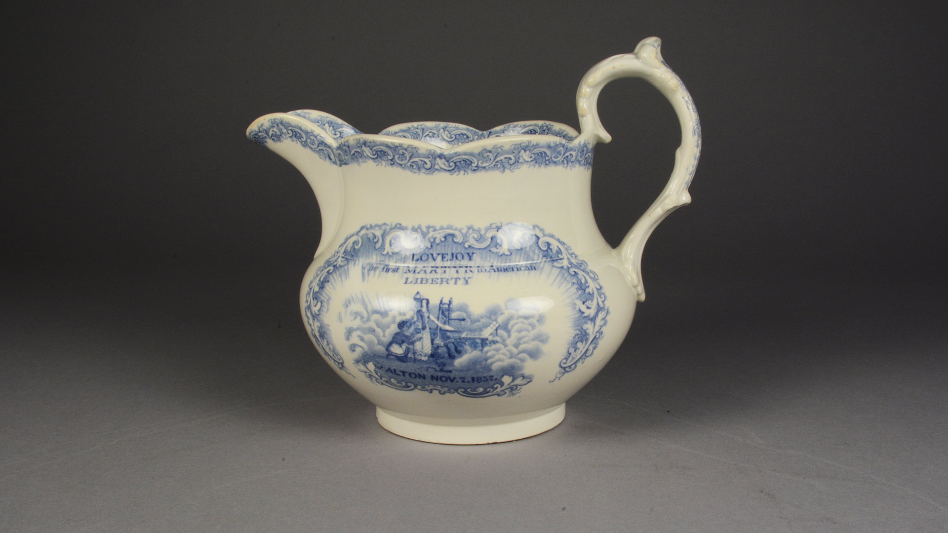 A white cermaic pitcher with blue detail depticting Elijah Lovejoy