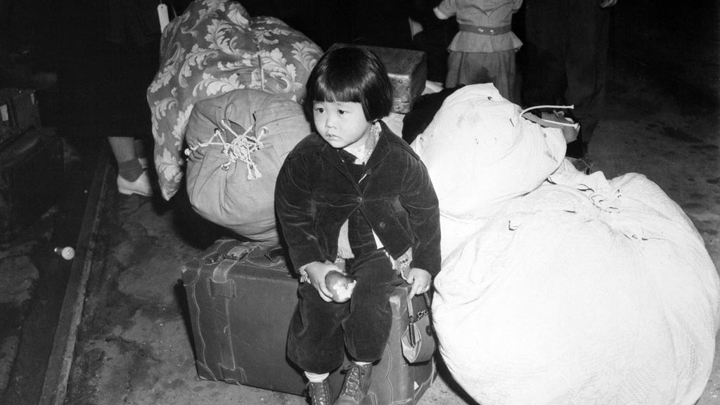 young Japanese girl sitting on a suitcase surrounded by large bags of luggage