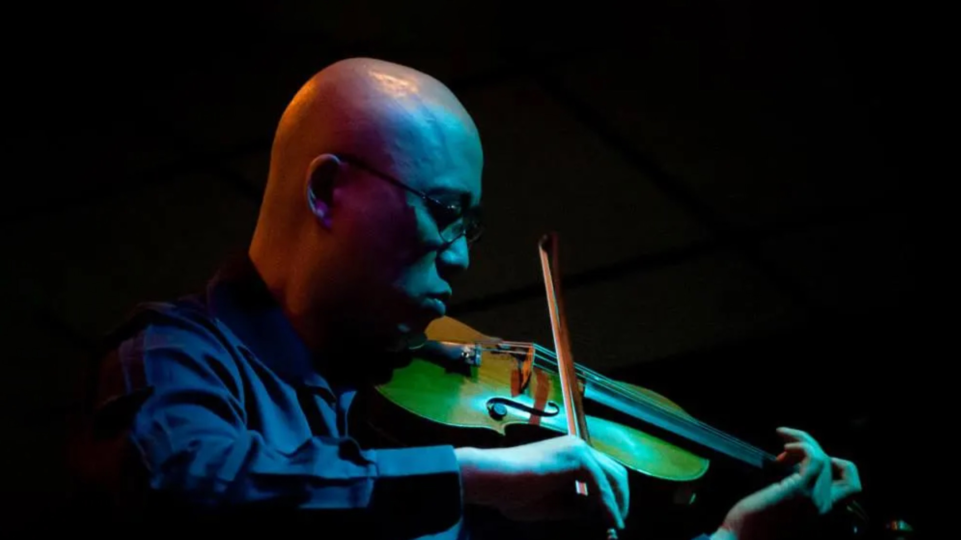 close-up of man playing the violin under blue ambient lighting