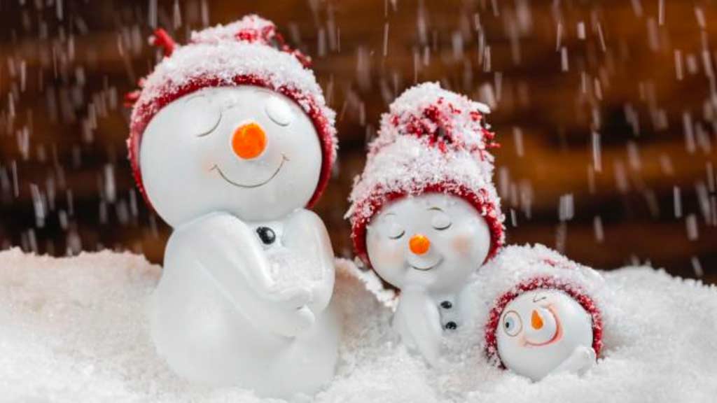 Three little snowmen smiling with their eyes closed and sitting on a pile of snow wearing red hats