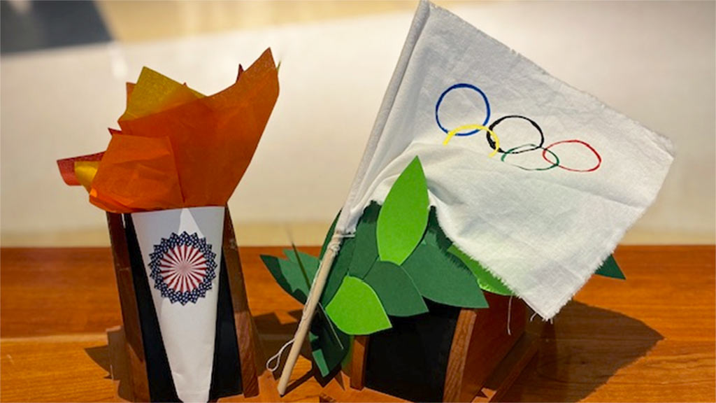 A paper craft imitation of the olympic torch, white flag, and a green leaf crown