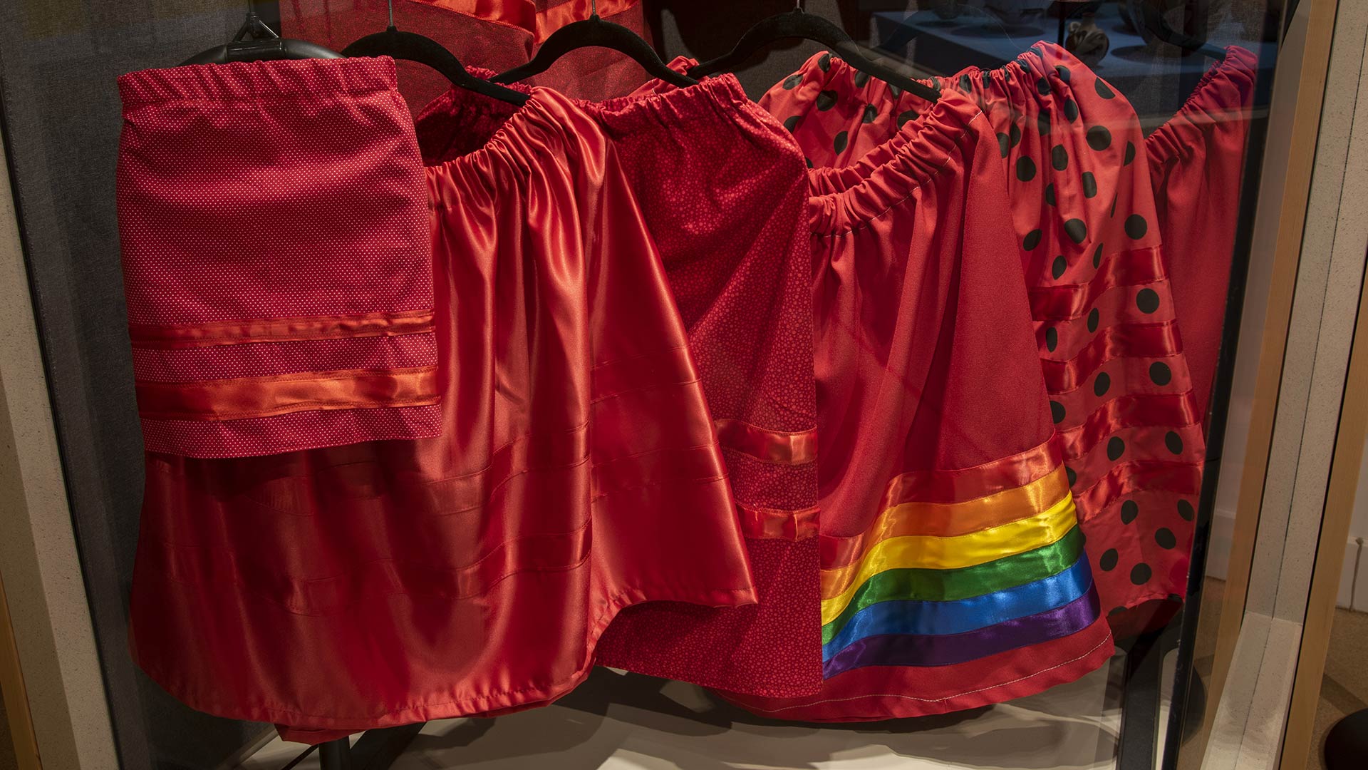 6 modern red garments (skirts and shirts) with various patterns in an exhibit case